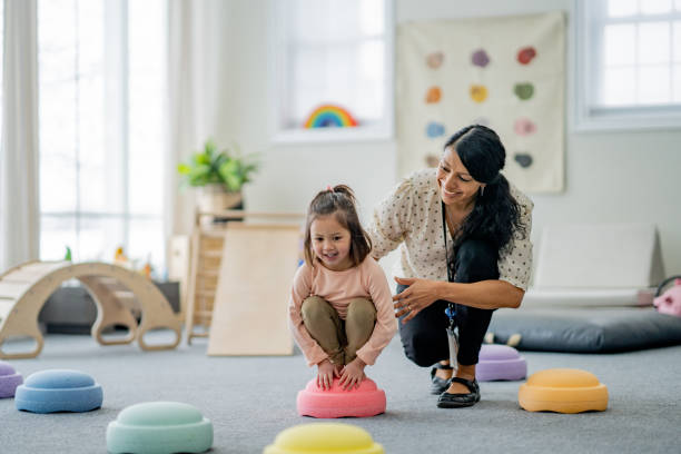 A clinician kneeling beside a young child on colorful stepping stones during a play- and movement-based session